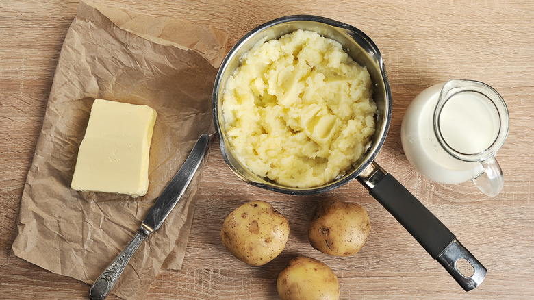 Mashed potatoes sit in a stainless steel pot surrounded by its ingredients