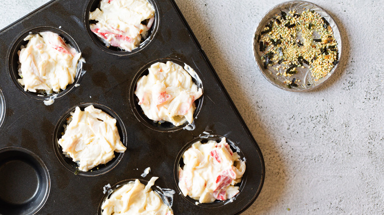 Unbaked sushi bake cups in muffin tins beside furikake