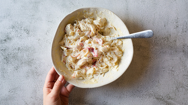 Hand holding a bowl with crab mixture and spoon