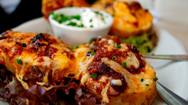Two loaded baked potatoes on a plate sit next to a bowl of sour cream and chives