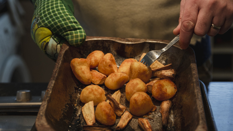 A person turns potatoes over with a fork inside a baking pan