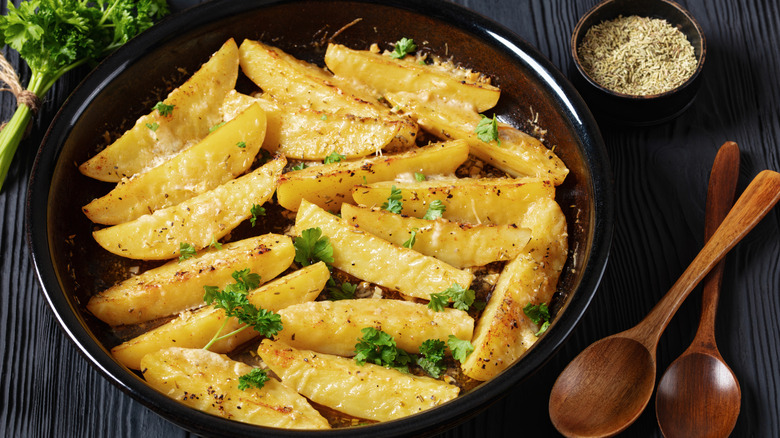 Greek-style lemon potato wedges sit on a brown plate next to wooden spoons