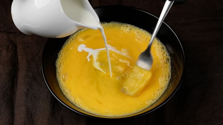 milk poured into bowl of raw eggs with fork