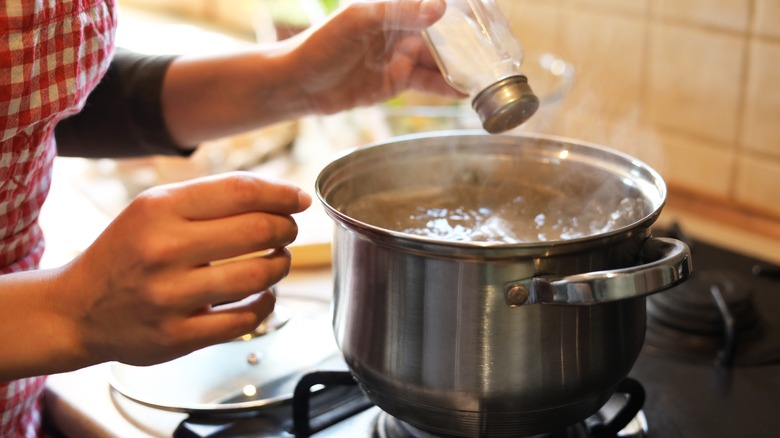 figure in red-and-white checked apron adding salt to pot