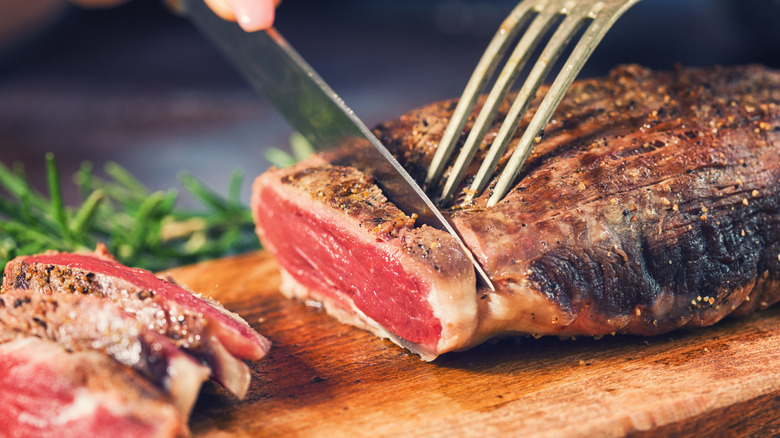 A hand slicing a steak with a knife and fork
