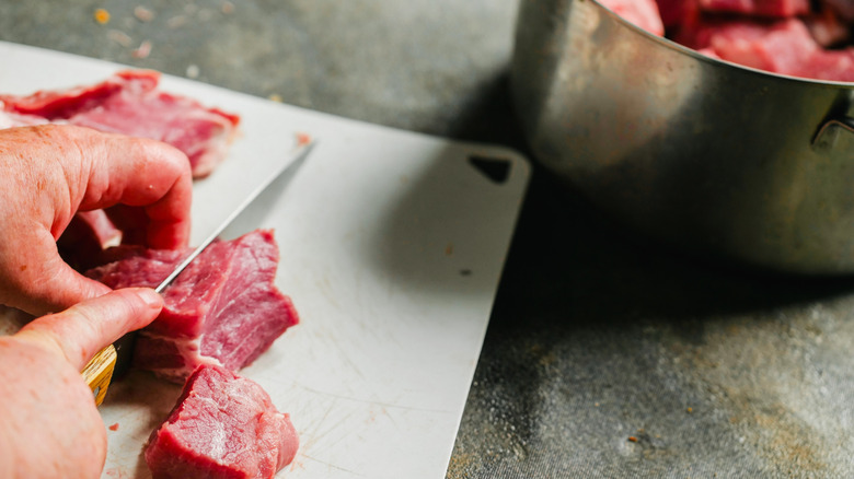 A hand slicing raw meat
