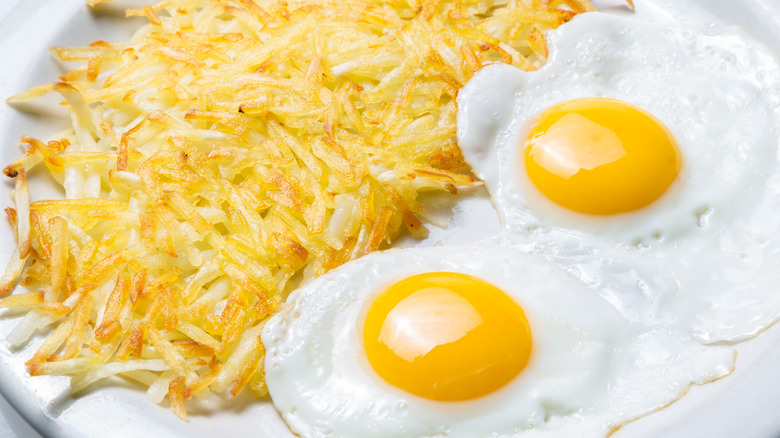 hash browns with fried eggs on white plate