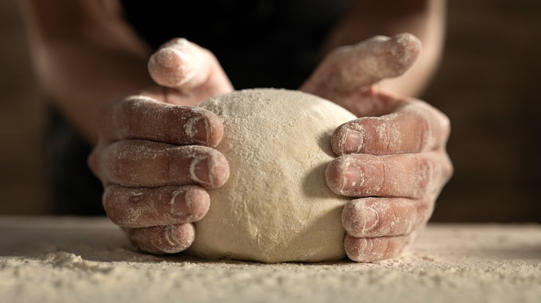 cook's hands around pizza dough