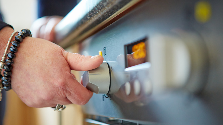 person's hand turning oven on