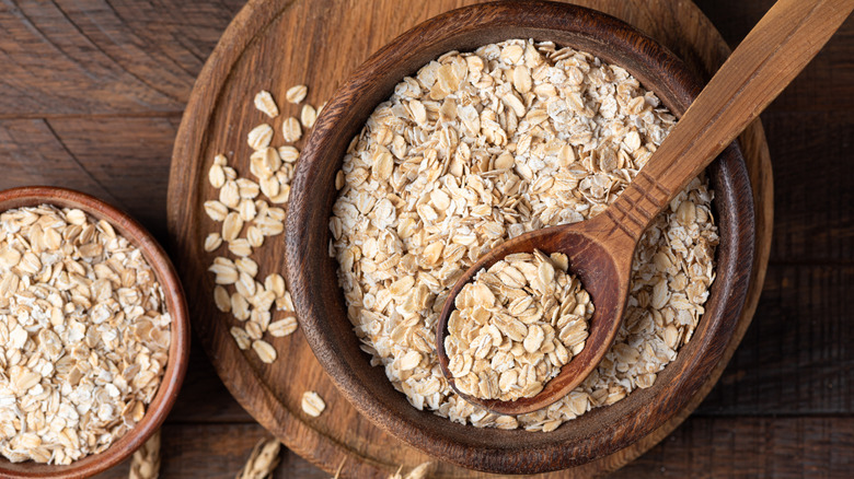 A bowl of oats with a wooden spoon next to another bowl of oats