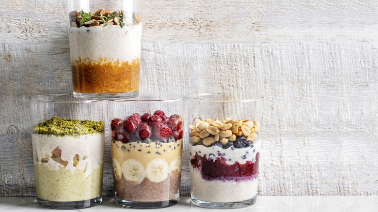 Four different overnight oats recipes in glasses against a white wall