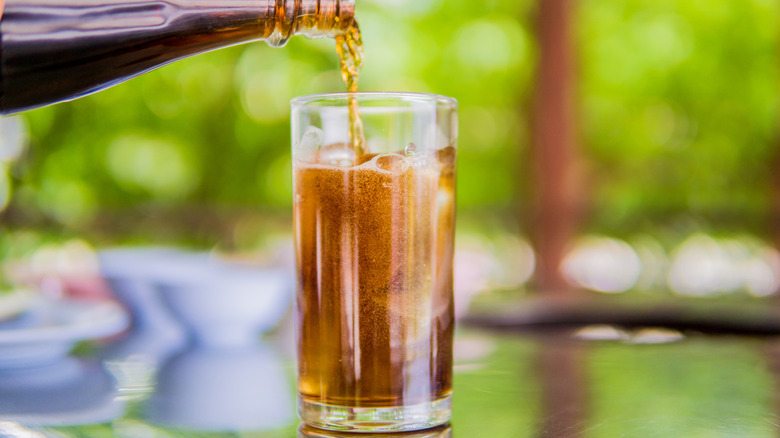 Person pouring Coke into glass with whiskey and ice.