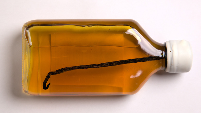a small glass bottle of whiskey with a vanilla bean inside it