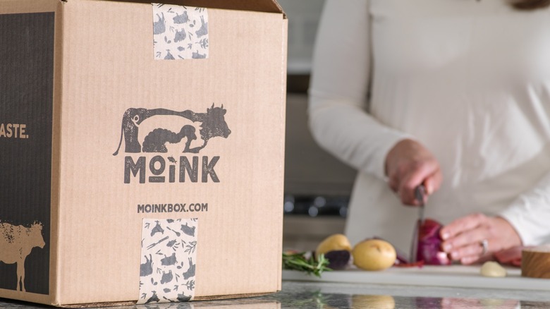 A box of Moink with person chopping in the background
