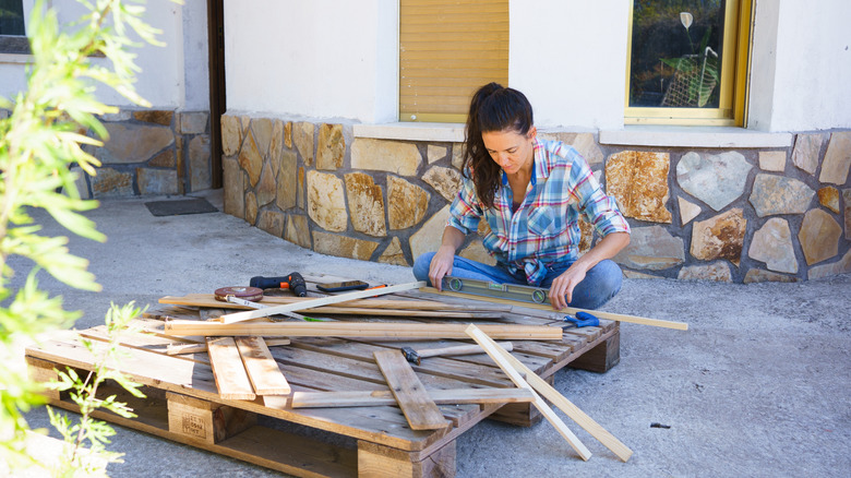 A home owner sits on the ground with tools next to a pallet.
