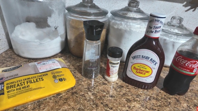 A small bottle of Coke sits next to a bottle of barbecue sauce, some spices, and chicken.