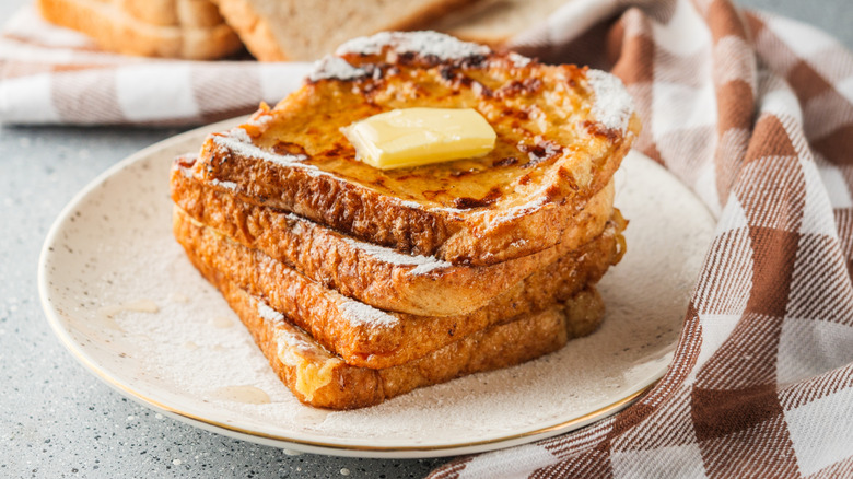 A stoneware plate with a stack of French toast topped with melting butter and syrup