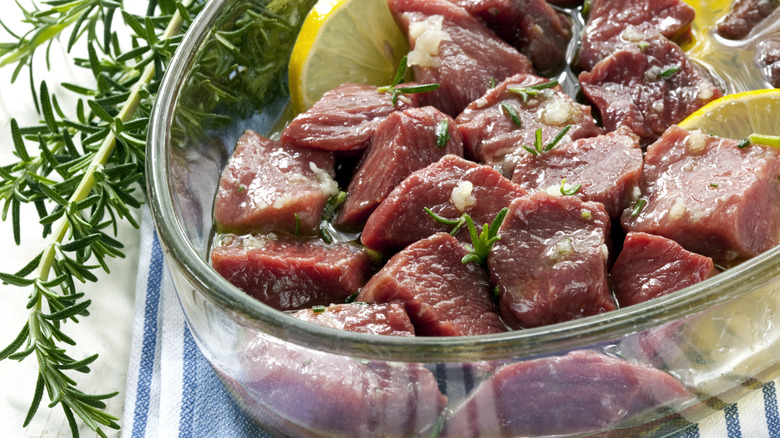 chunks of beef chuck marinating in a bowl with lemon, garlic, and fresh rosemary