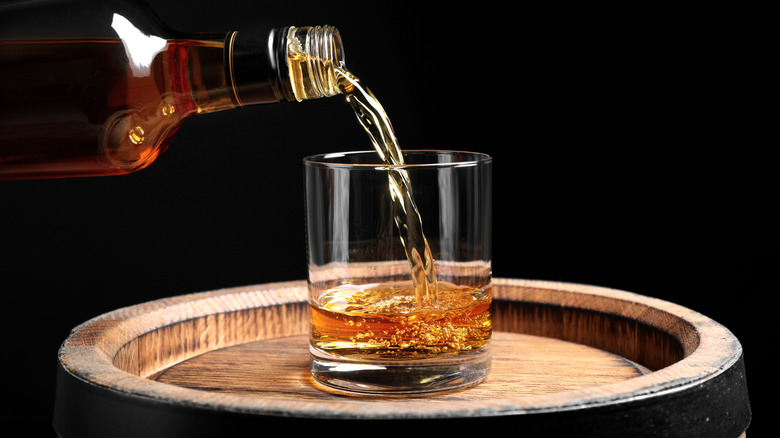 Whisky poured into glass on barrel