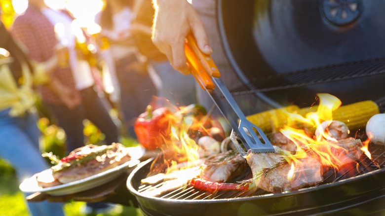Group of friends having a cookout preparing grilled meats and vegetables