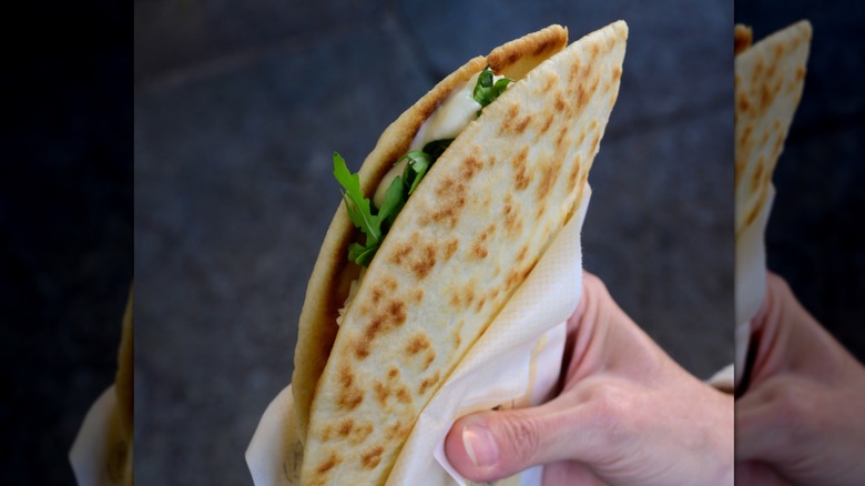 A hand holding a thin Italian flatbread sandwich