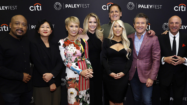 The regular cast of Shark Tank Sharks standing on a red carpet and smiling