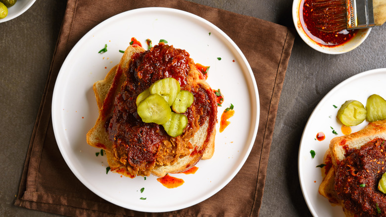 Nashville hot chicken topped with pickle chip on white bread with bowl of hot sauce beside it
