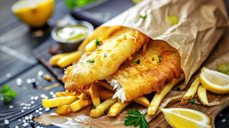 Battered fish and chips on black table with garnish