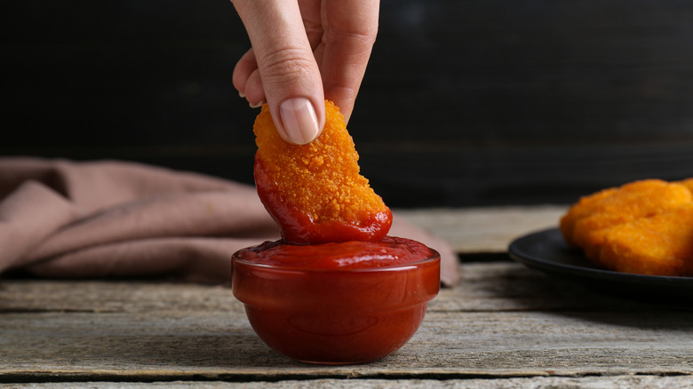 Hand dipping a chicken nugget into ketchup