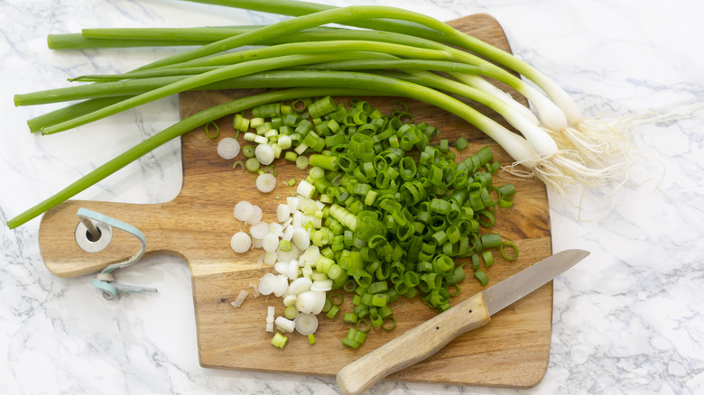 Overview of chopped and whole scallions on a cutting board with a knife