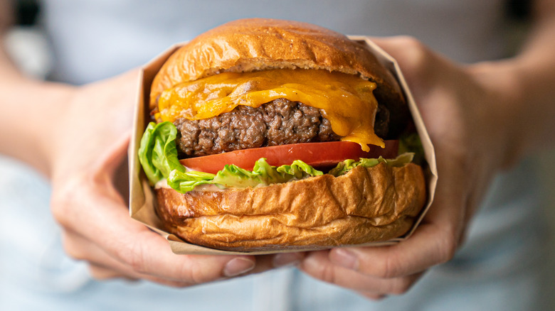 Closeup of hands holding a juicy cheeseburger
