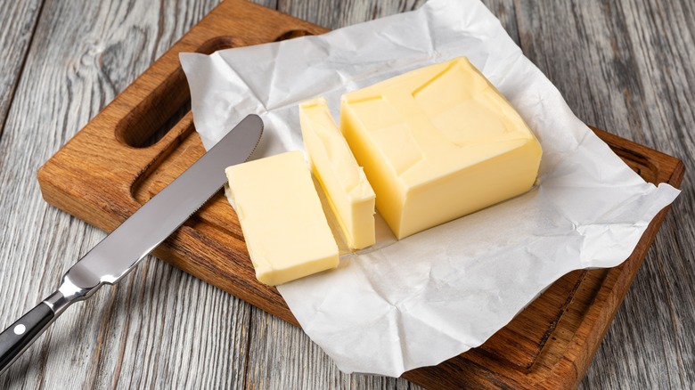 An unwrapped block of butter sits on a wooden cutting board next to a butter knife
