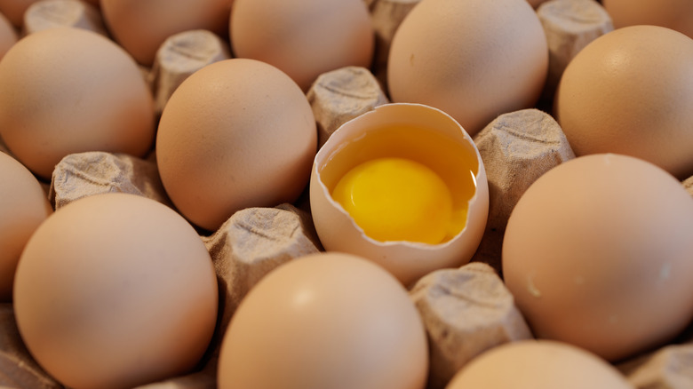 Close up of a carton of eggs with one cracked open