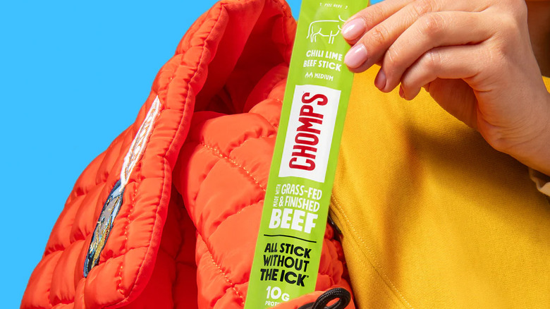 Someone holds a Chomps Chili Lime Beef Snack Stick.