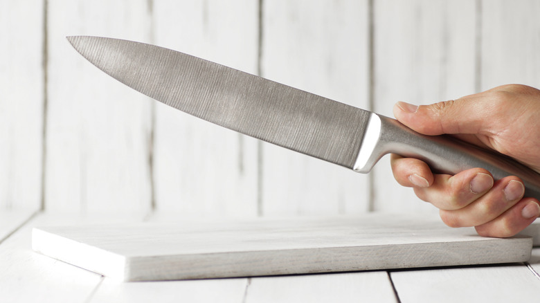 Hand holding sharp chef knife over a cutting board