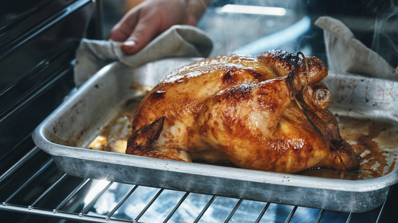A home chef places a rotisserie chicken into an oven on a stainless steel baking dish