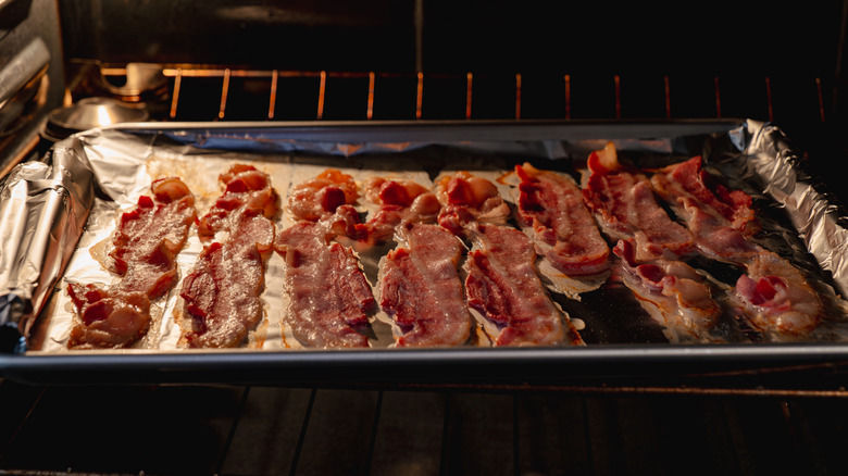 Long pieces of bacon bake on a foil-lined tray in the oven