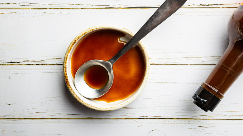 Small bowl of Worcestershire sauce with a spoon and an empty bottle
