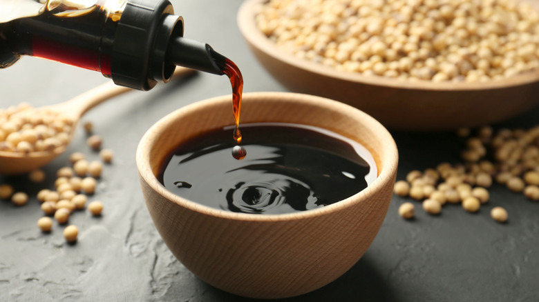 Pouring soy sauce into a small bamboo bowl with dried soy beans