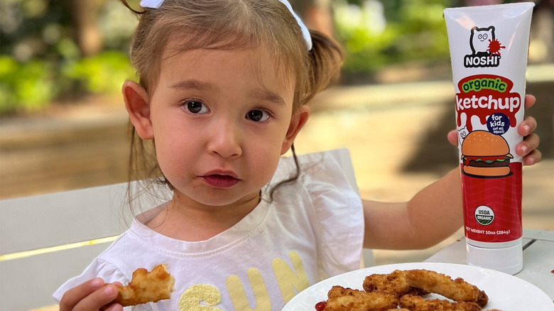 Kid holding Noshi organic ketchup product and eating chicken