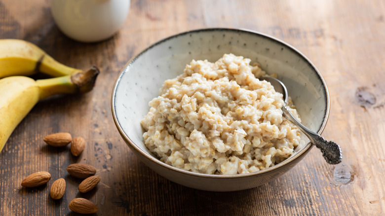 Homemade oatmeal sits in a bowl with a spoon, with almonds, bananas, and milk nearby