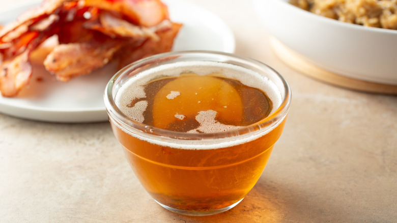 A jar of liquid bacon grease sits next to a plate of bacon.
