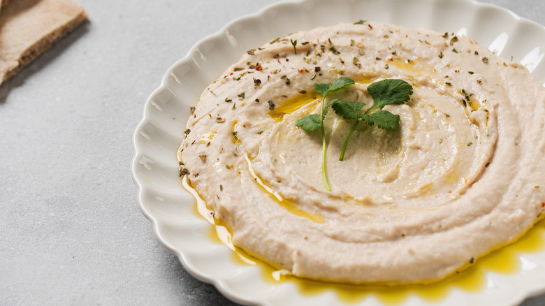 Hummus on a white plate with an herb garnish