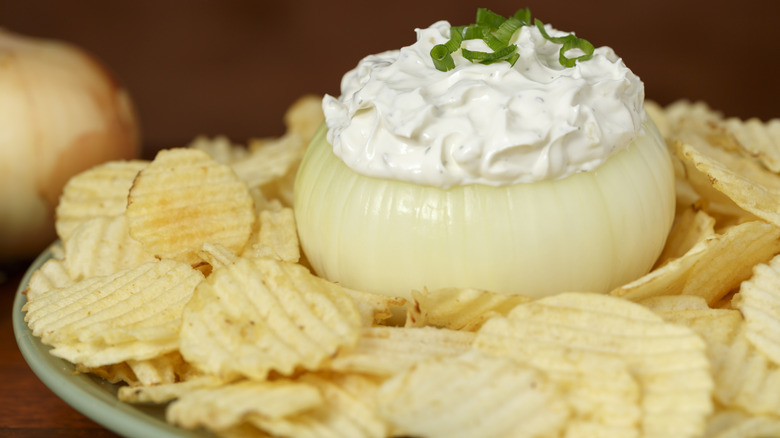 Onion dip in a hollow-out white onion on a plate with potato chips