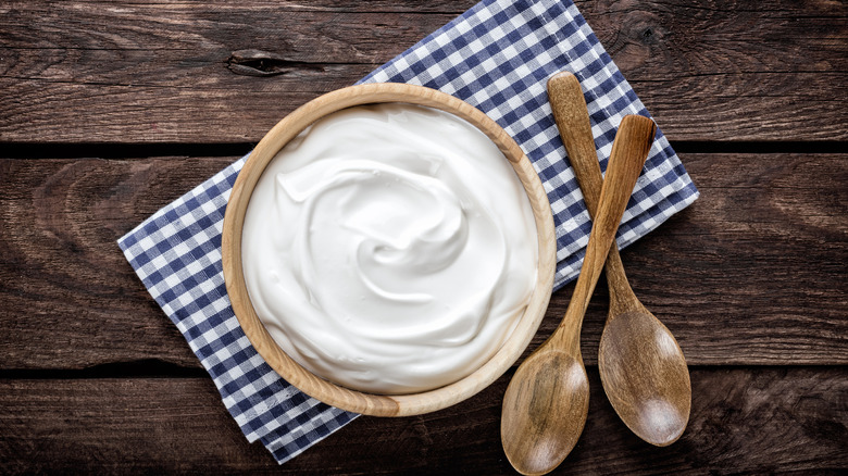 A wooden bowl of sour cream sits on a checkered cloth, with two wooden spoons sitting adjacent.
