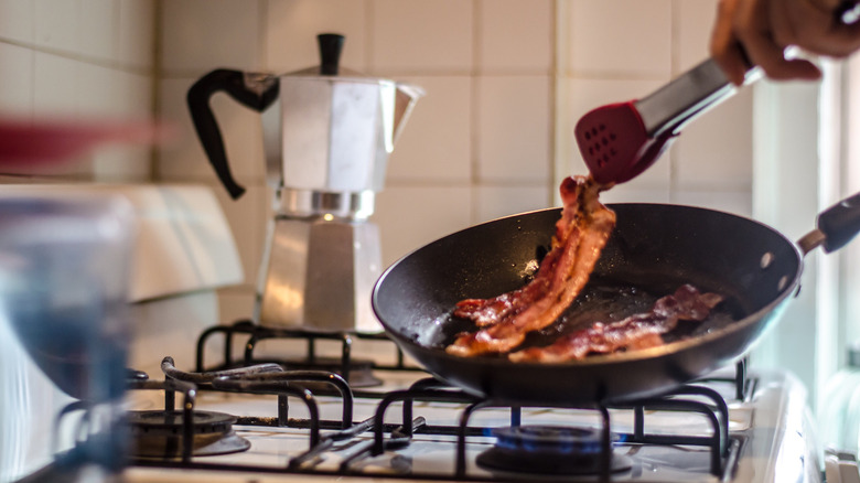 Someone cooks bacon on the stovetop in a kitchen