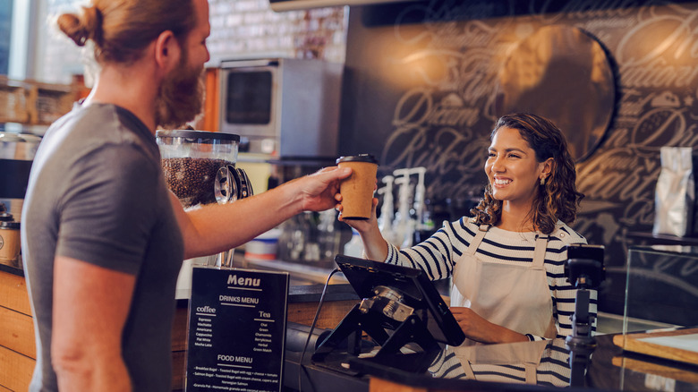 A smiling barista hands a coffee cup to a customer