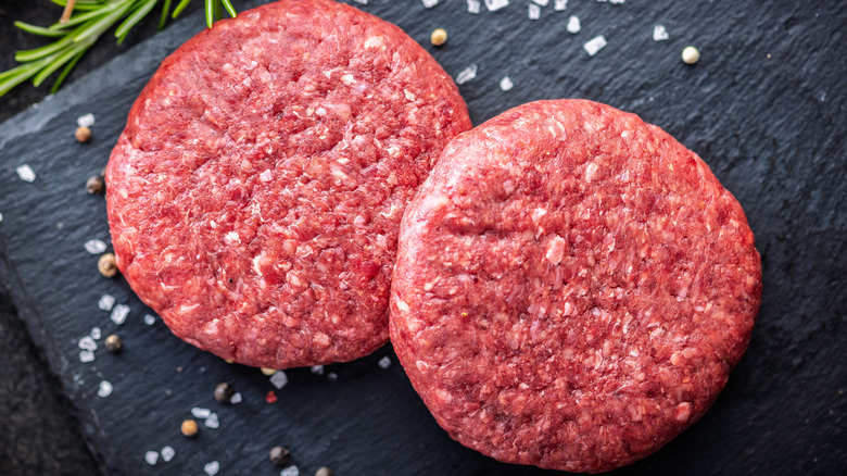 Two raw burger patties on a black slab