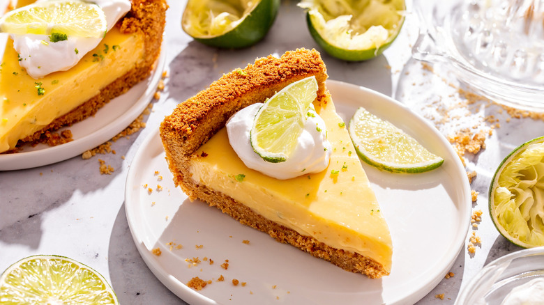 Slices of key lime pie on white plates surrounded by limes