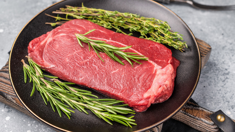 A raw top sirloin steak with fresh herbs.